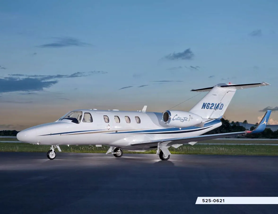 A white Cessna CitationJet + with blue and gold stripes is parked on a tarmac at dusk.