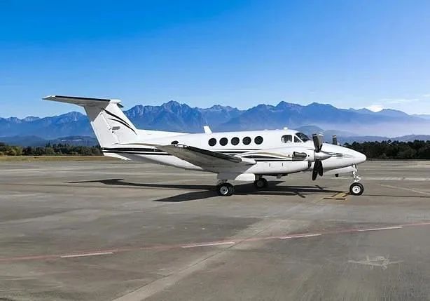A white Beechcraft King Air turboprop aircraft with black and gold stripes is parked on a tarmac under a clear blue sky.
