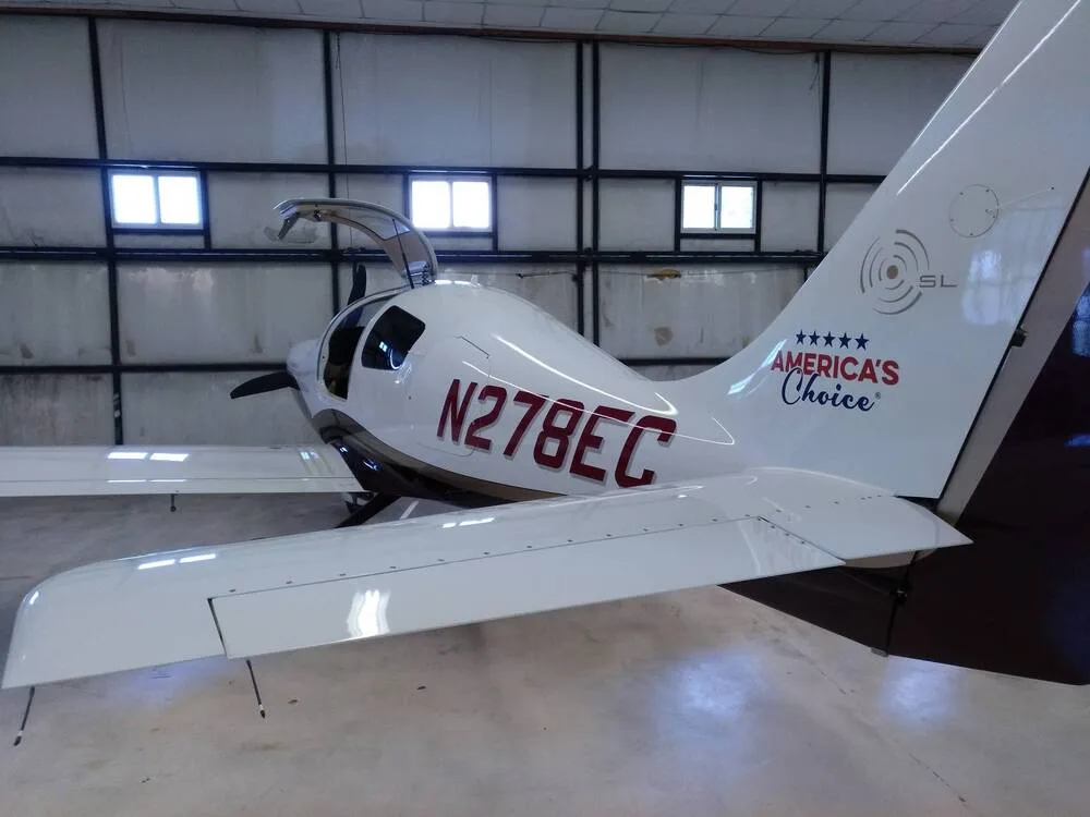 The tail and right wing of a white and brown Cirrus SR22 aircraft, N278EC, inside a hangar.