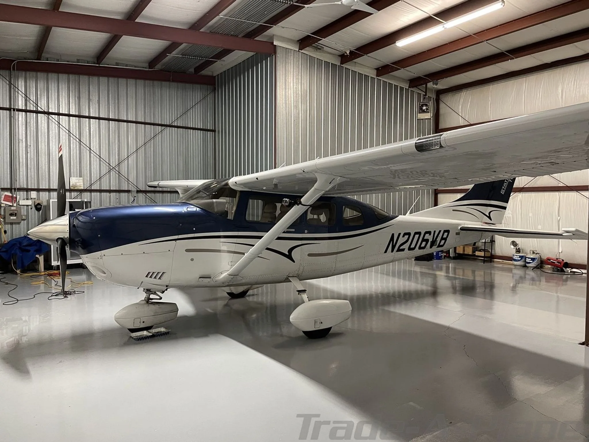 A side view of a blue and white Cessna 182 aircraft with registration N206VB, parked in a hangar.