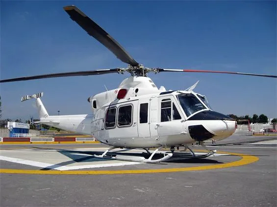 A white Bell 412 helicopter with a black nose is parked on a helipad under a clear blue sky.