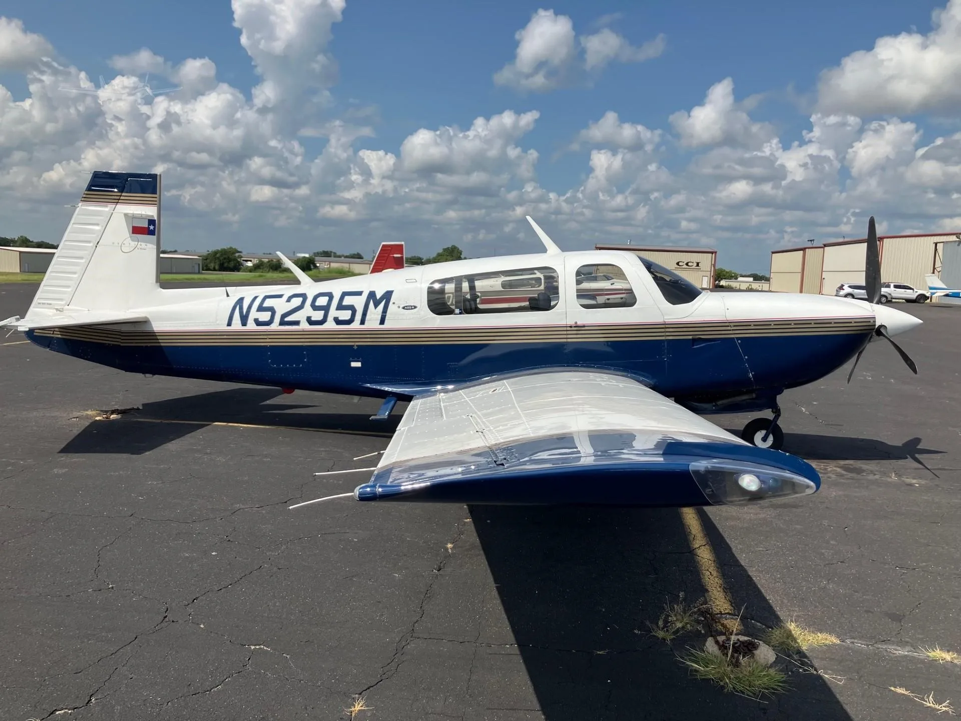 A blue and white single-engine aircraft with registration N5295M and a Texas flag on its tail, parked on an airport tarmac.