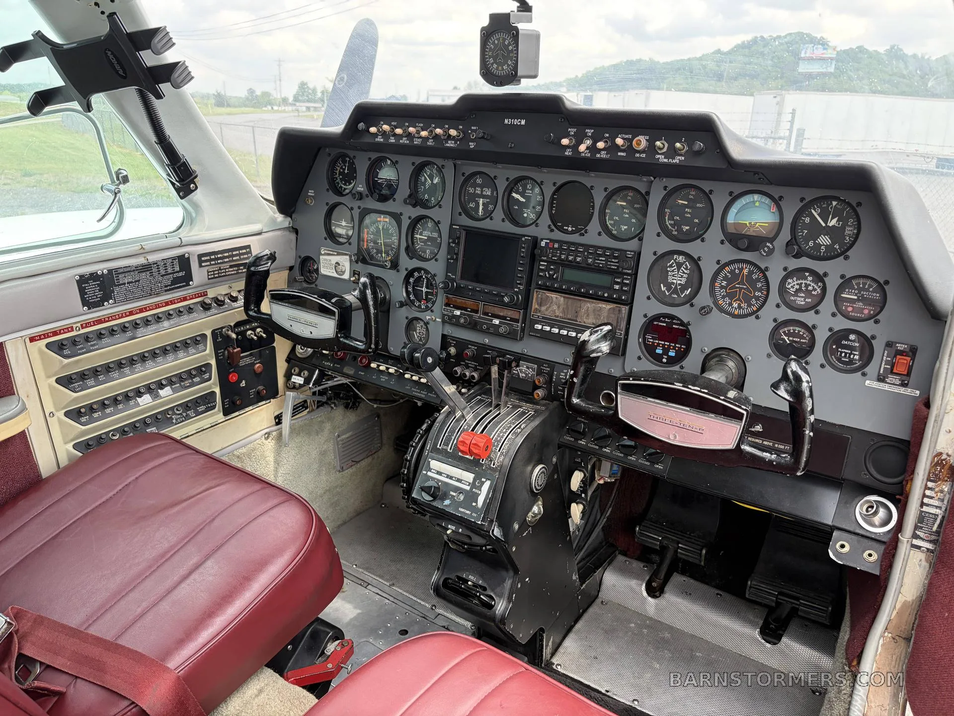 A wider view of the twin-engine aircraft cockpit, featuring the instrument panel, yokes, and red leather seats.