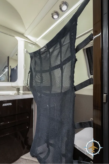 A black mesh cargo net hanging in an aircraft cabin, next to a dark wood-paneled wall.