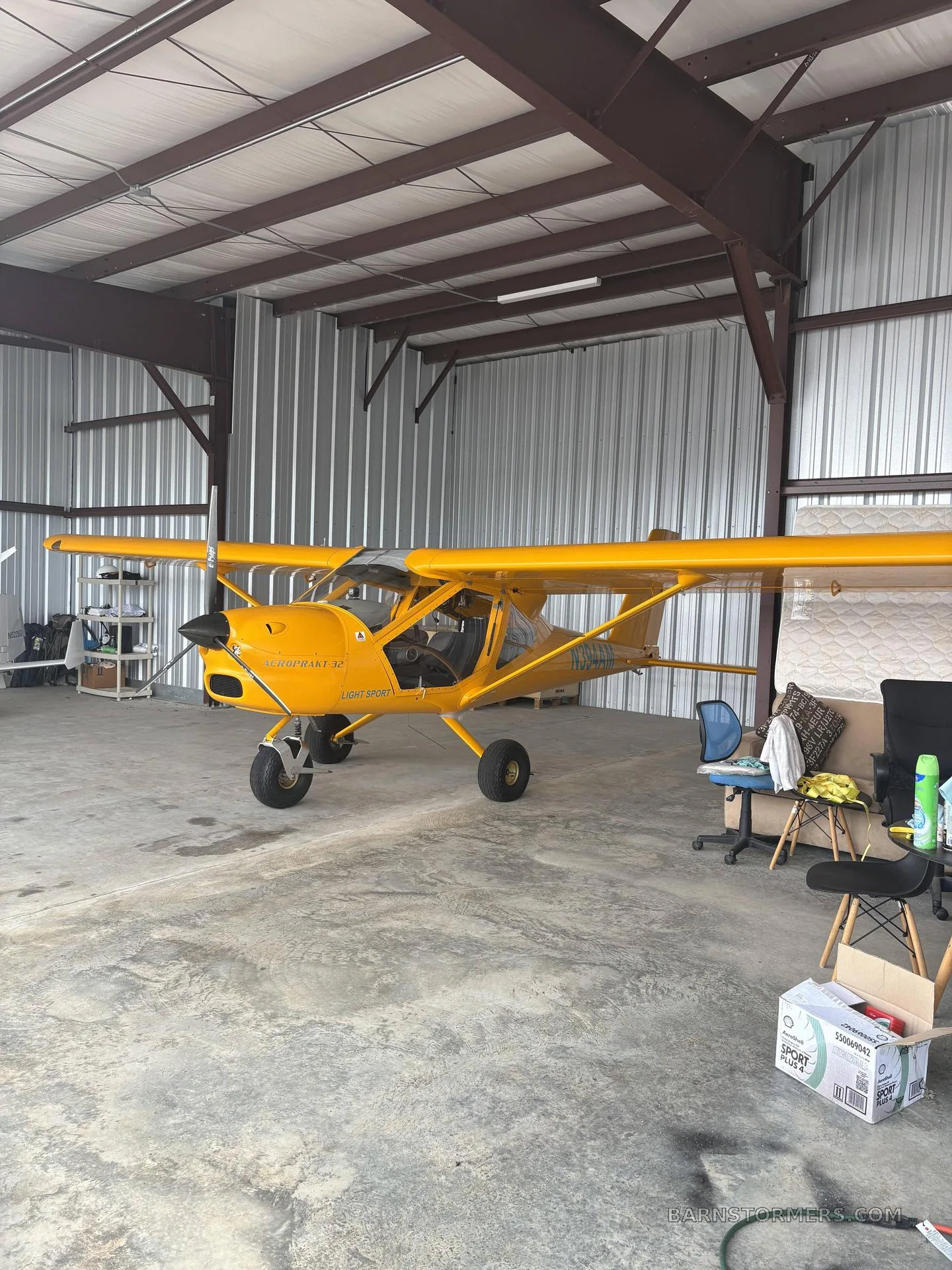 A bright yellow Aeroprakt A-32 Light Sport aircraft is parked inside a metal hangar.