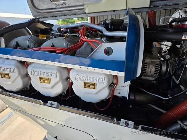 A close-up view of a Continental aircraft engine with its cowling open, showing cylinders and red ignition wires.