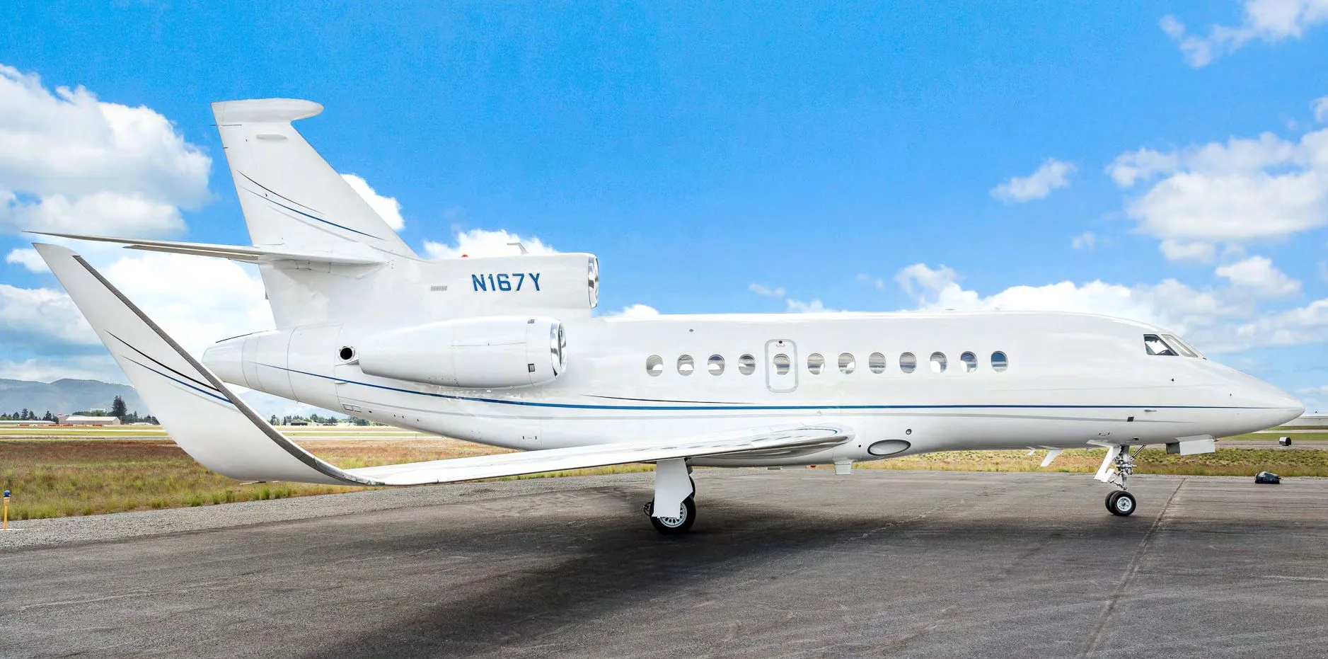 A side view of a white Dassault Falcon 900EX business jet, registration N167Y, on an airfield.