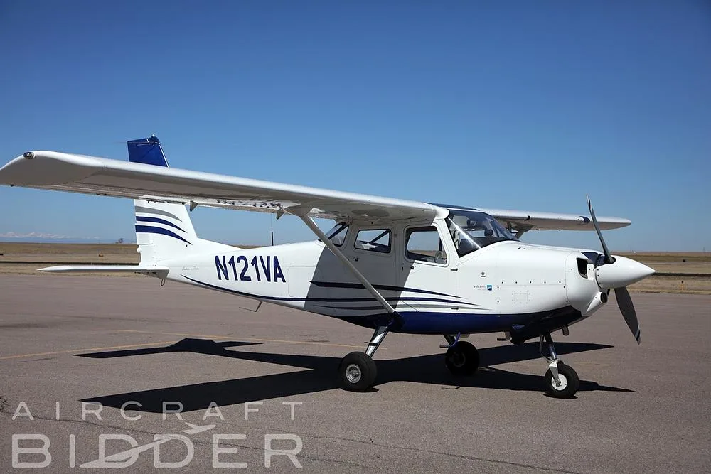 A white and blue Tecnam P2010 single-engine aircraft, N121VA, parked on an asphalt runway under a clear blue sky.
