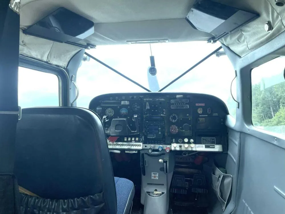 The cockpit of a small aircraft, showing the instrument panel, yoke, and pilot's seat from a wider angle.
