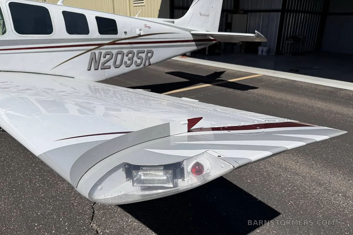 A close-up view of the wingtip of a white Beechcraft Baron, showing the navigation lights and part of the fuselage with registration N2035R.