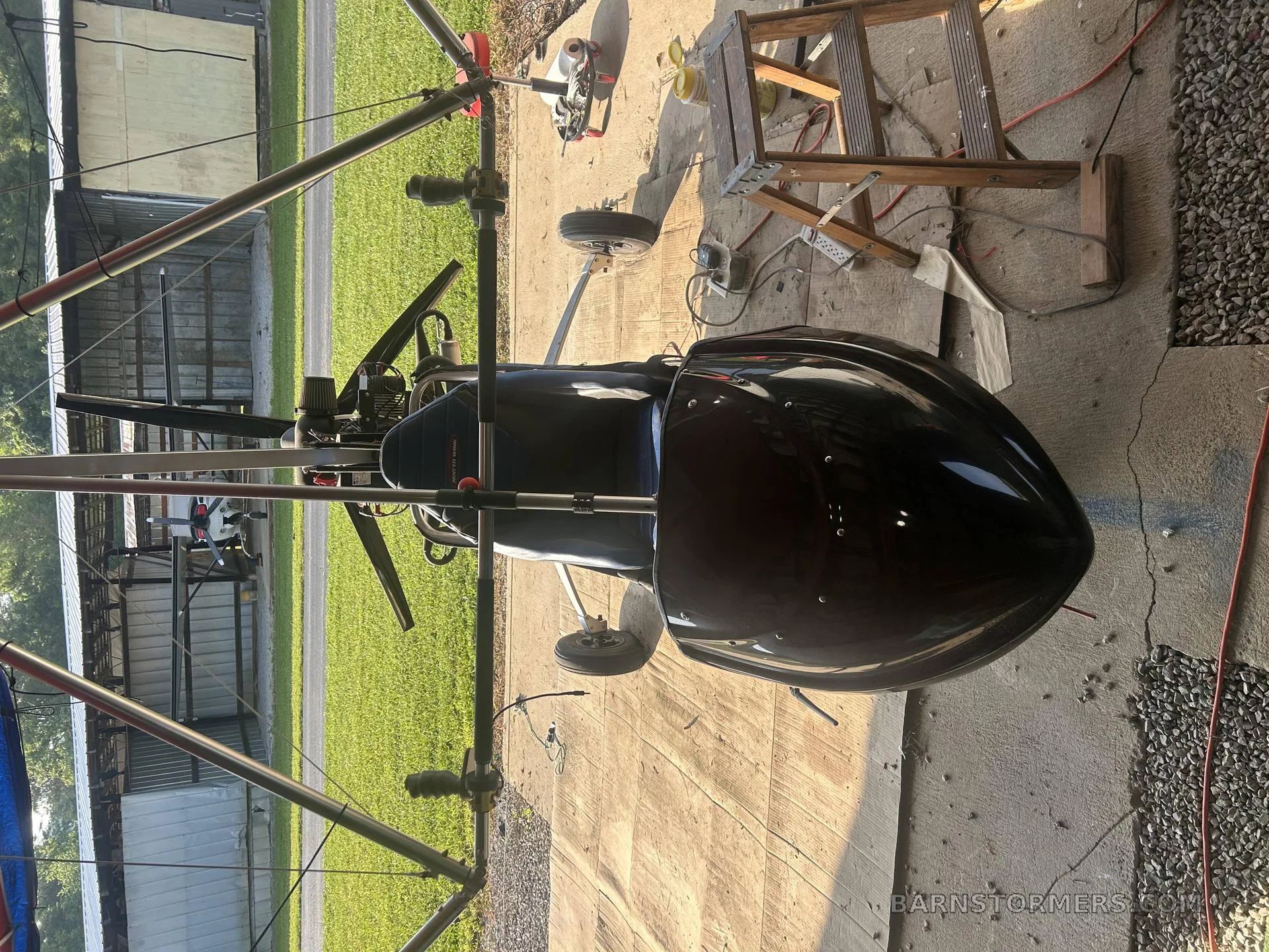 A black ultralight autogyro with a single seat and exposed frame, parked on a concrete pad.