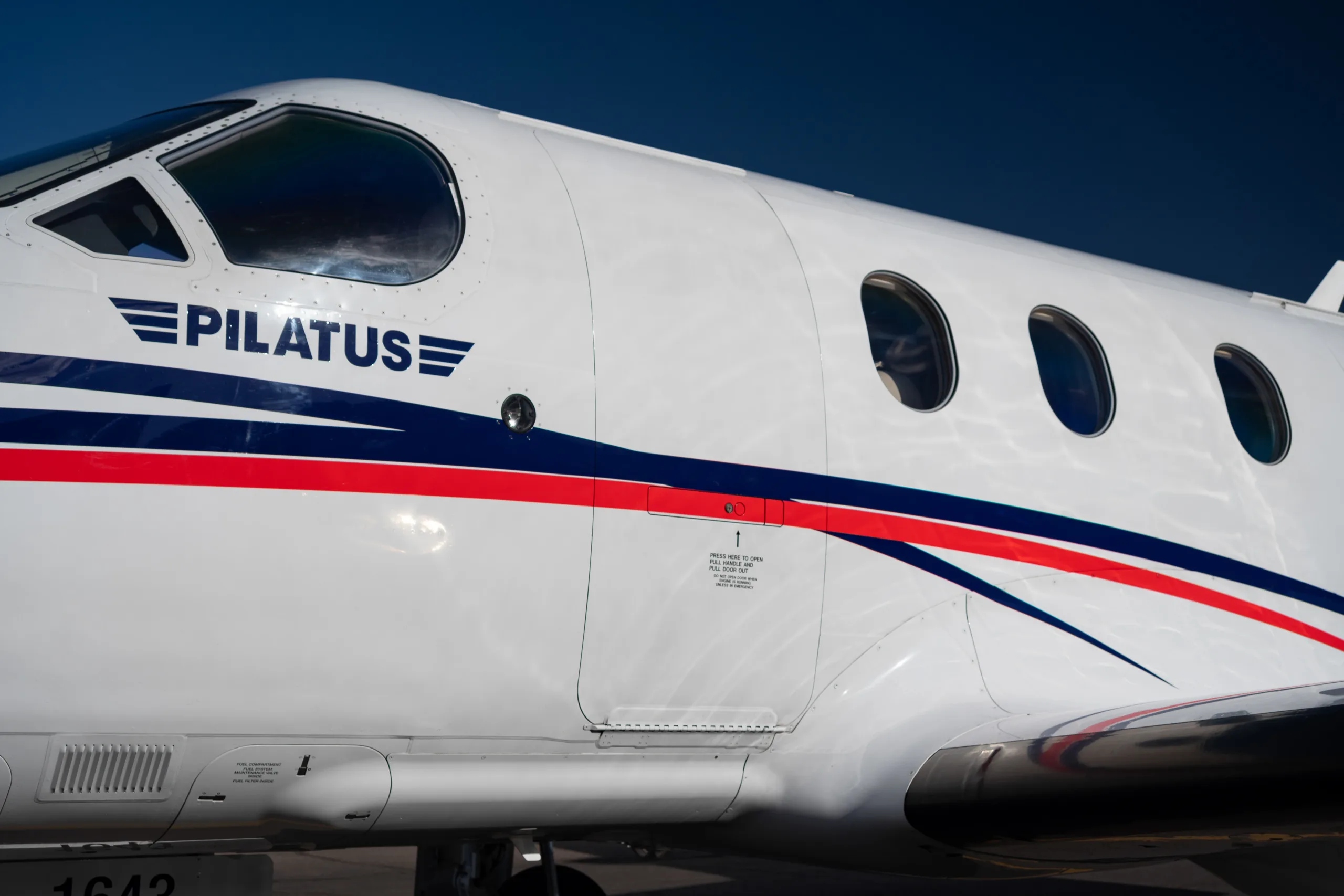 A close-up view of the fuselage of the Pilatus PC-12 aircraft, N985AW, showing the "PILATUS" logo and passenger windows.