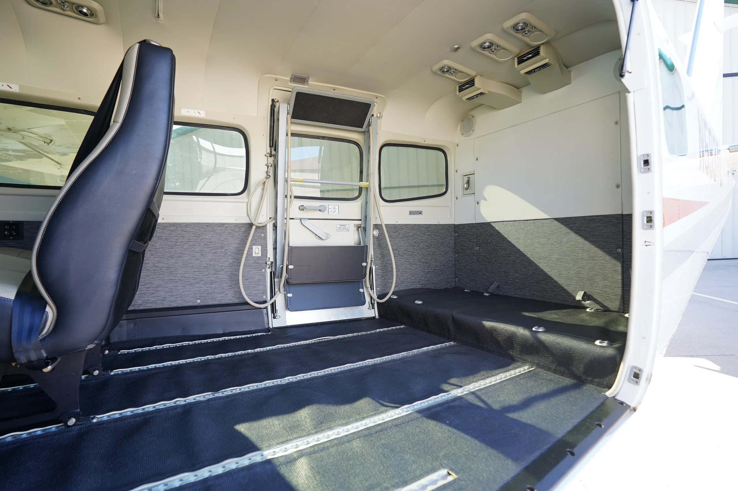 The aircraft's interior cabin with the side door open, showing cargo rails on the floor and most seats removed.