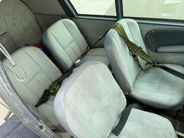 The light gray interior cabin seats with olive green seatbelts of a small aircraft.