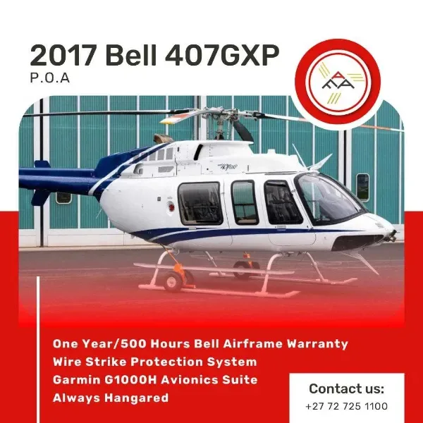 A white Bell 407GXP helicopter with blue stripes is parked on an apron in front of a hangar.