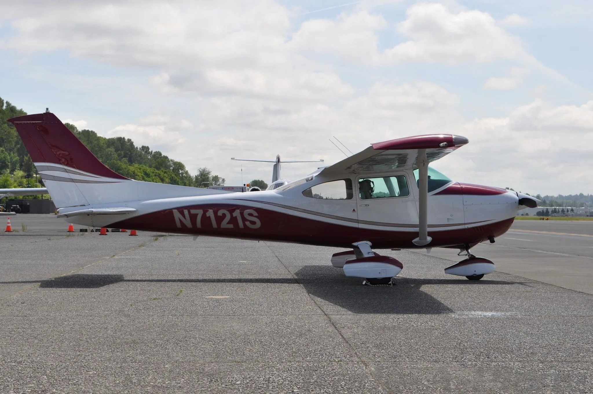A red and white Cessna N7121S is parked on an airfield, viewed from the side.