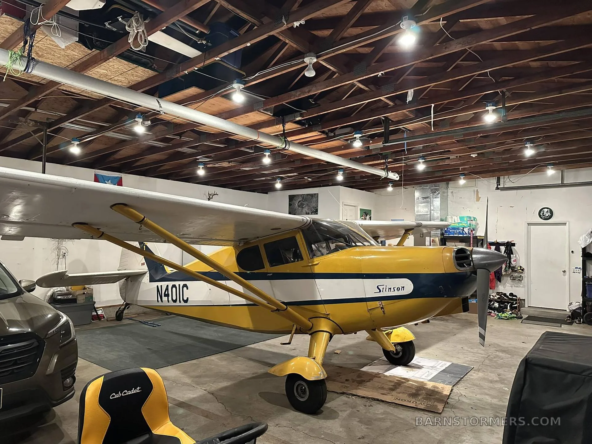 A front-side view of the yellow and blue Stinson aircraft, N401C, in a garage.