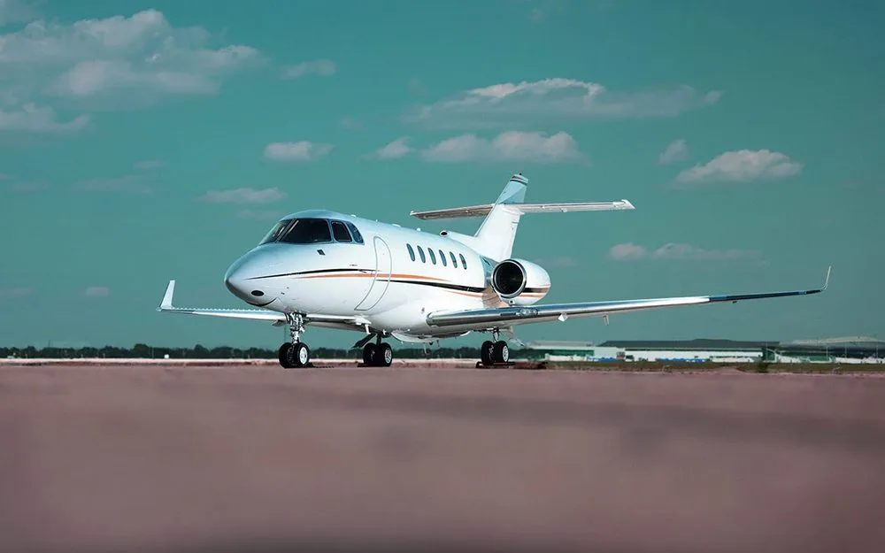 A white private jet with gold and black accents is parked on a tarmac under a blue sky.