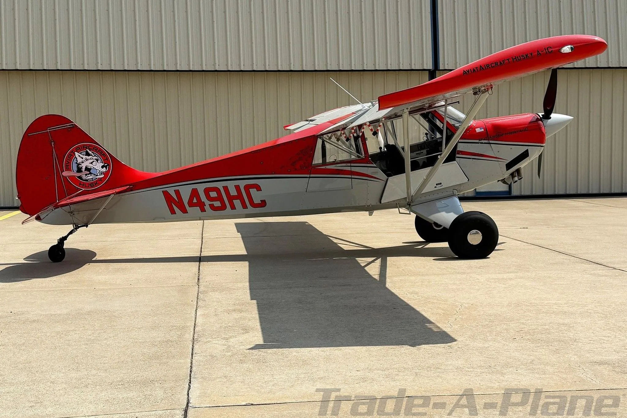 A side profile of the red and white Aviat Husky A-1C aircraft, registration N49HC, on an airfield.
