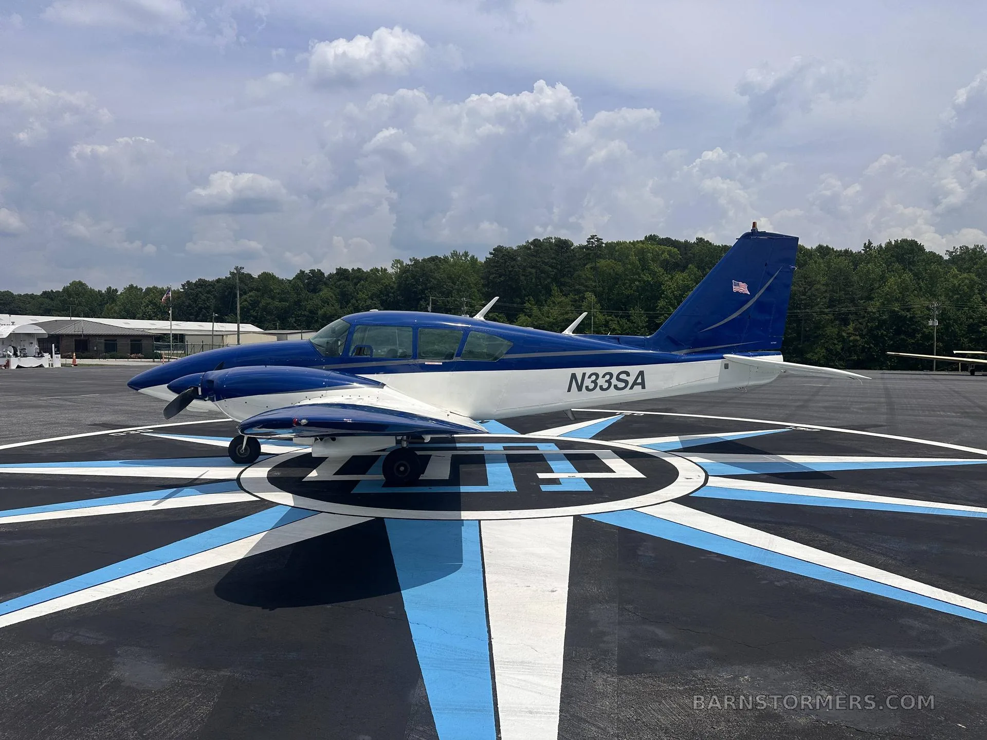 A three-quarter front view of a blue and white single-engine aircraft (N33SA) parked on a compass rose marking on an airfield.