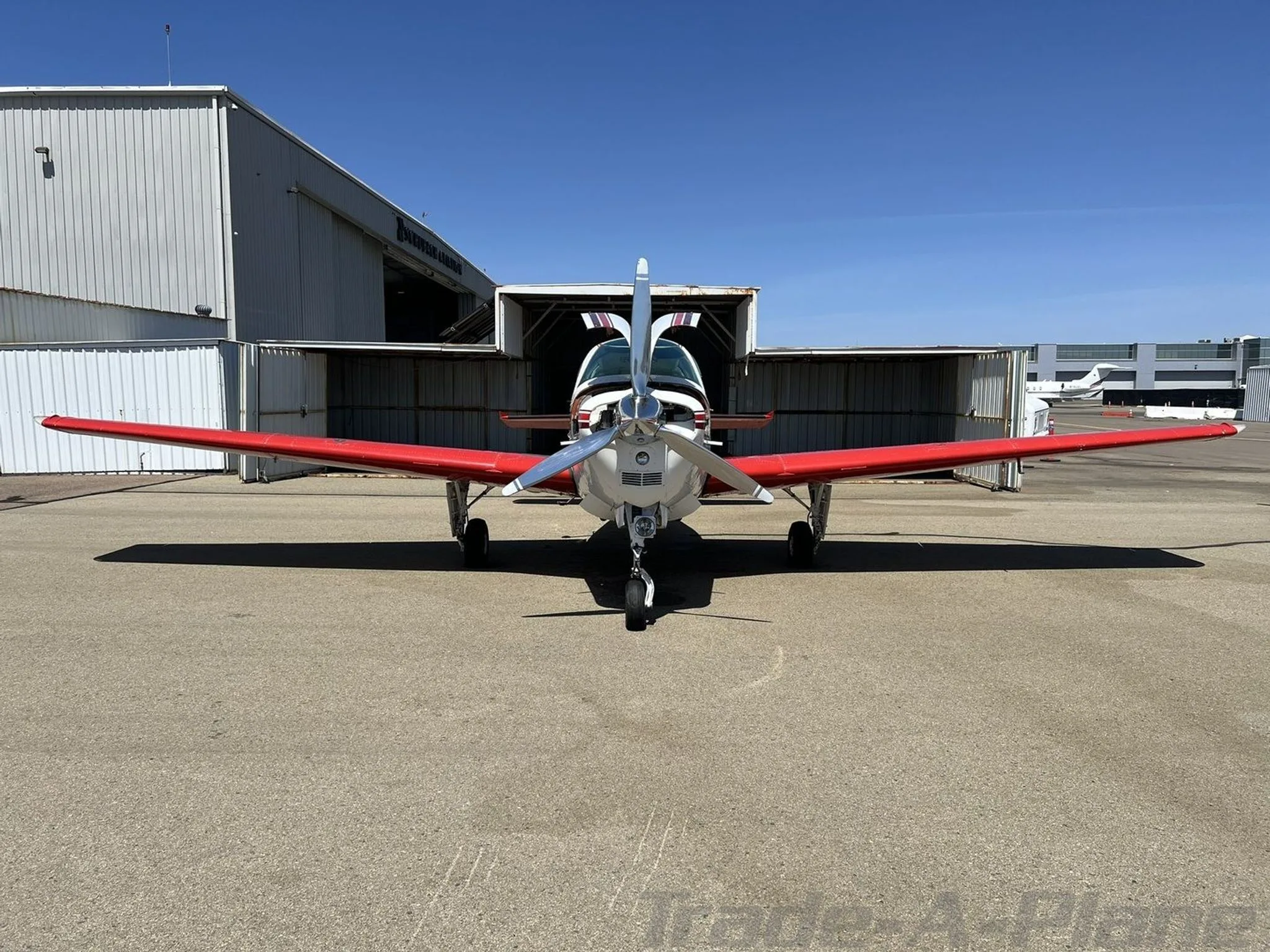 Frontal view of a white and red Beechcraft Bonanza with a polished propeller, parked on an airfield.