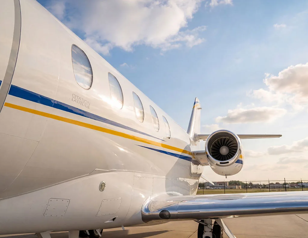 A close-up view of the fuselage and engine of a white Cessna Citation Latitude, showing the blue and yellow stripe detail.