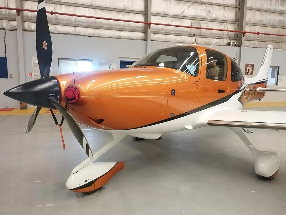 A close-up front view of an orange and white Cirrus SR22 aircraft inside a hangar.