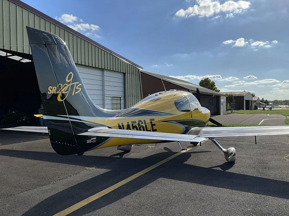 Rear view of a yellow and black Cirrus SR22 aircraft with registration N456LE parked outside a hangar.