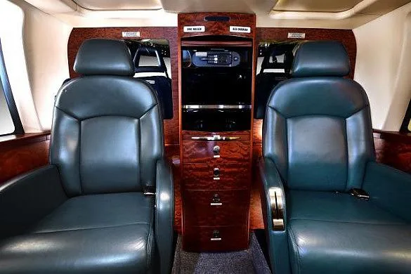 Two dark grey leather passenger seats face each other with a wooden cabinet between them in an aircraft cabin.
