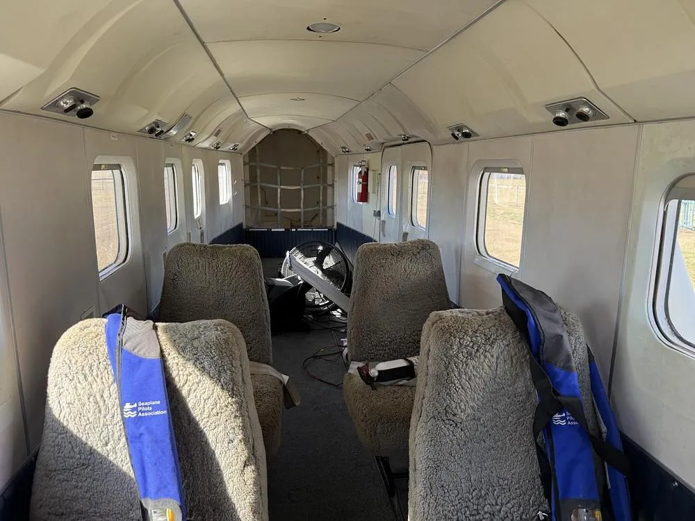 The interior cabin of an aircraft with several sheepskin-covered seats and equipment in the rear.