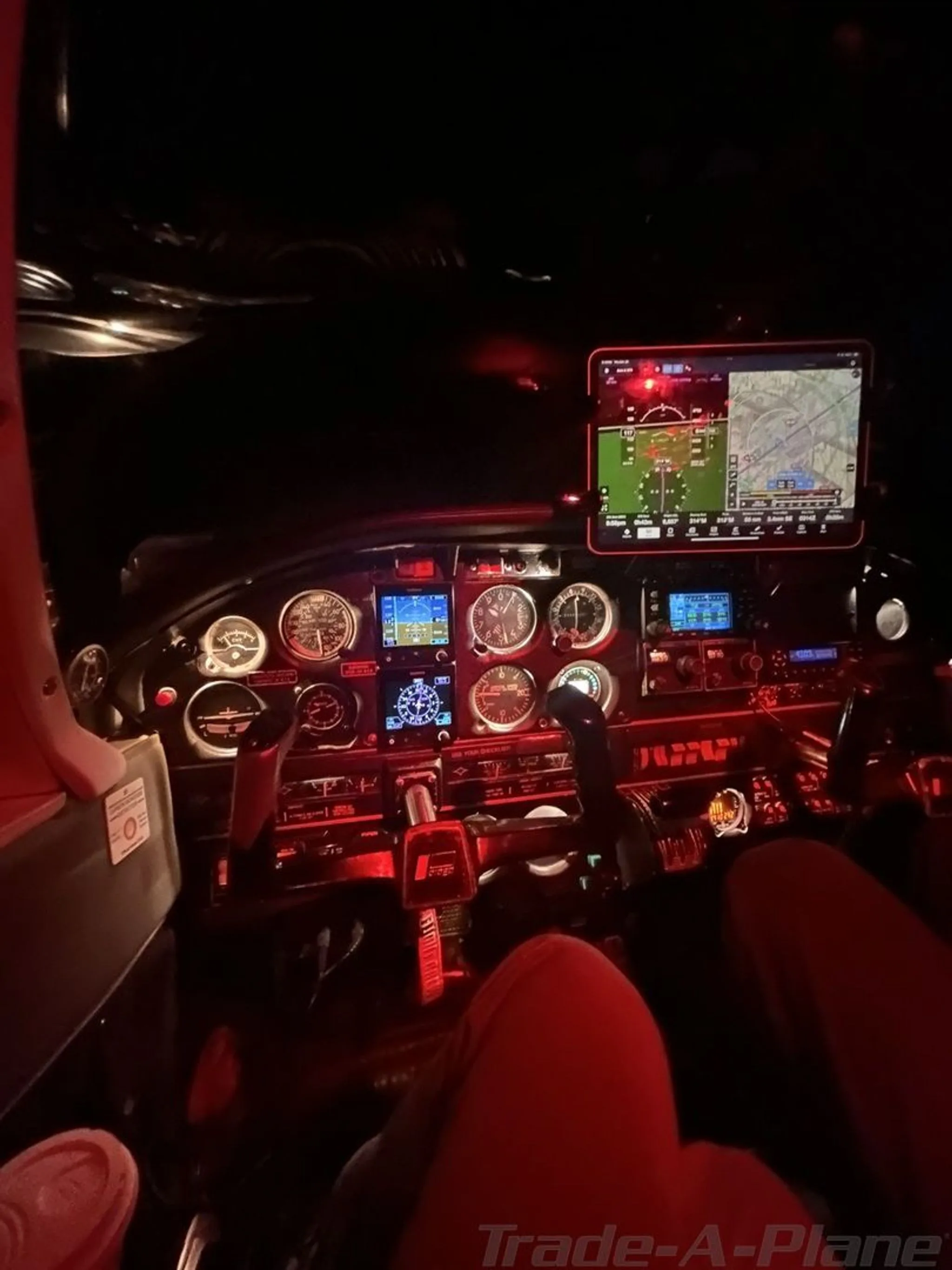 The cockpit instrument panel of a Piper aircraft illuminated with red light, showing a tablet mounted on the right.