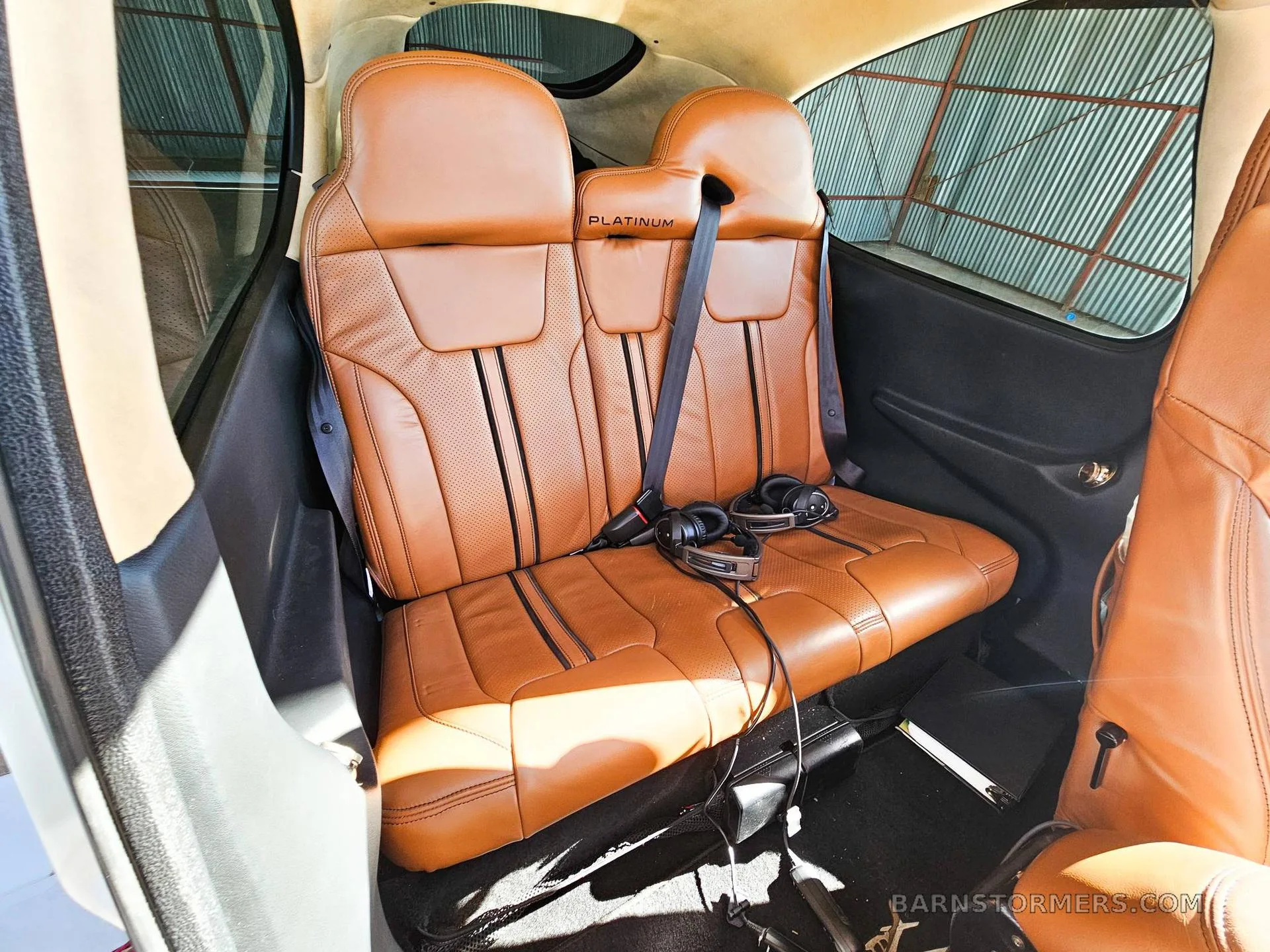 The tan leather rear passenger seats of a Cirrus aircraft, with "PLATINUM" embossed on the headrests.