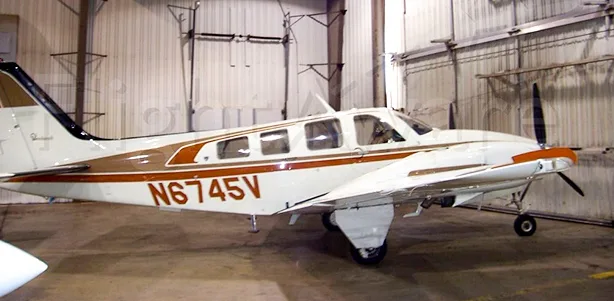 A white and brown Beechcraft Bonanza with the tail number N6745V is parked inside a hangar.