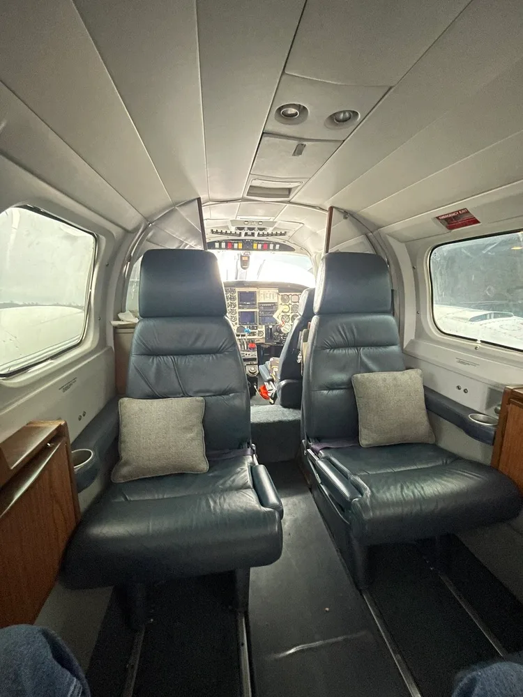 The aircraft cabin interior with two rows of dark leather seats and a view into the cockpit.