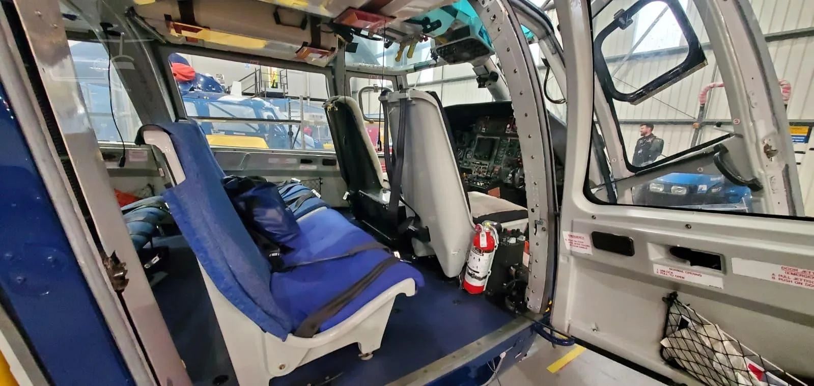 The Airbus H155 helicopter cabin interior with blue seats, a fire extinguisher, and a view into the cockpit.
