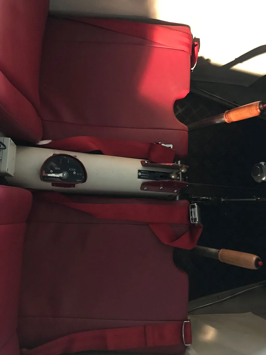The red upholstered seats and central control stick of a small aircraft cabin.