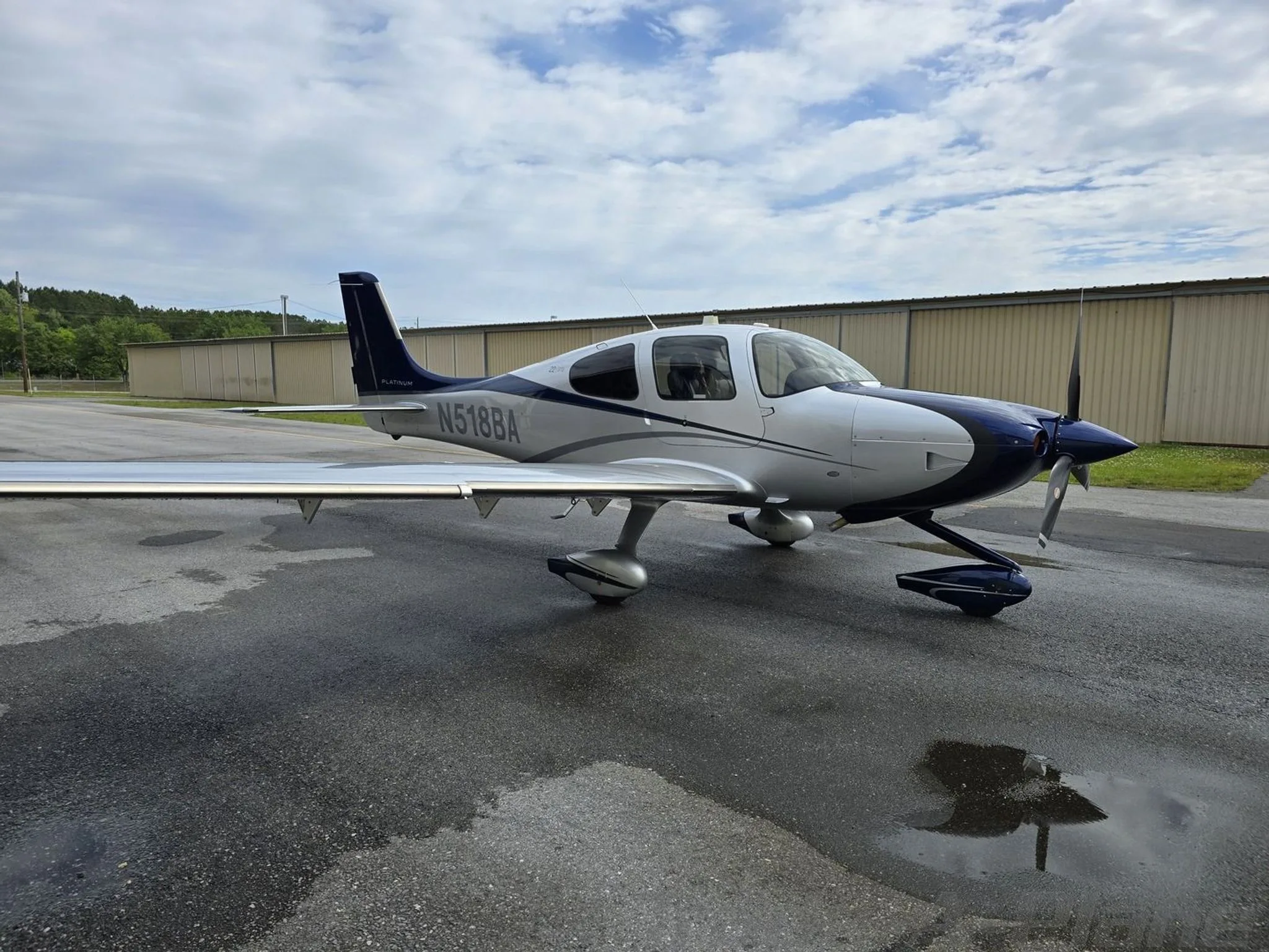 A Cirrus SR22T aircraft with a blue and silver paint scheme, registration N518BA, parked on a wet tarmac.