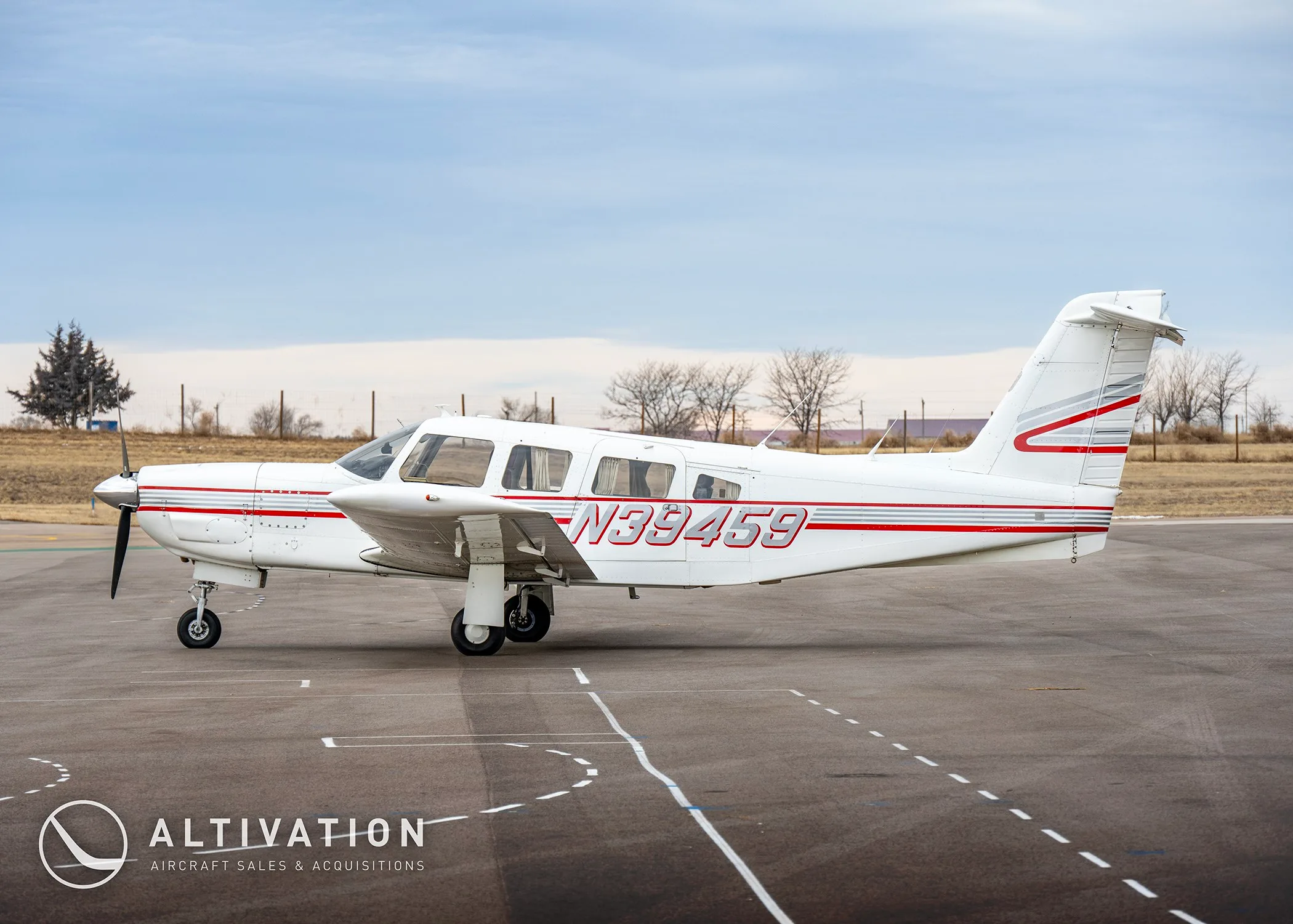 A white single-engine propeller aircraft with red and grey stripes, tail number N39459, seen from the side on an airfield.