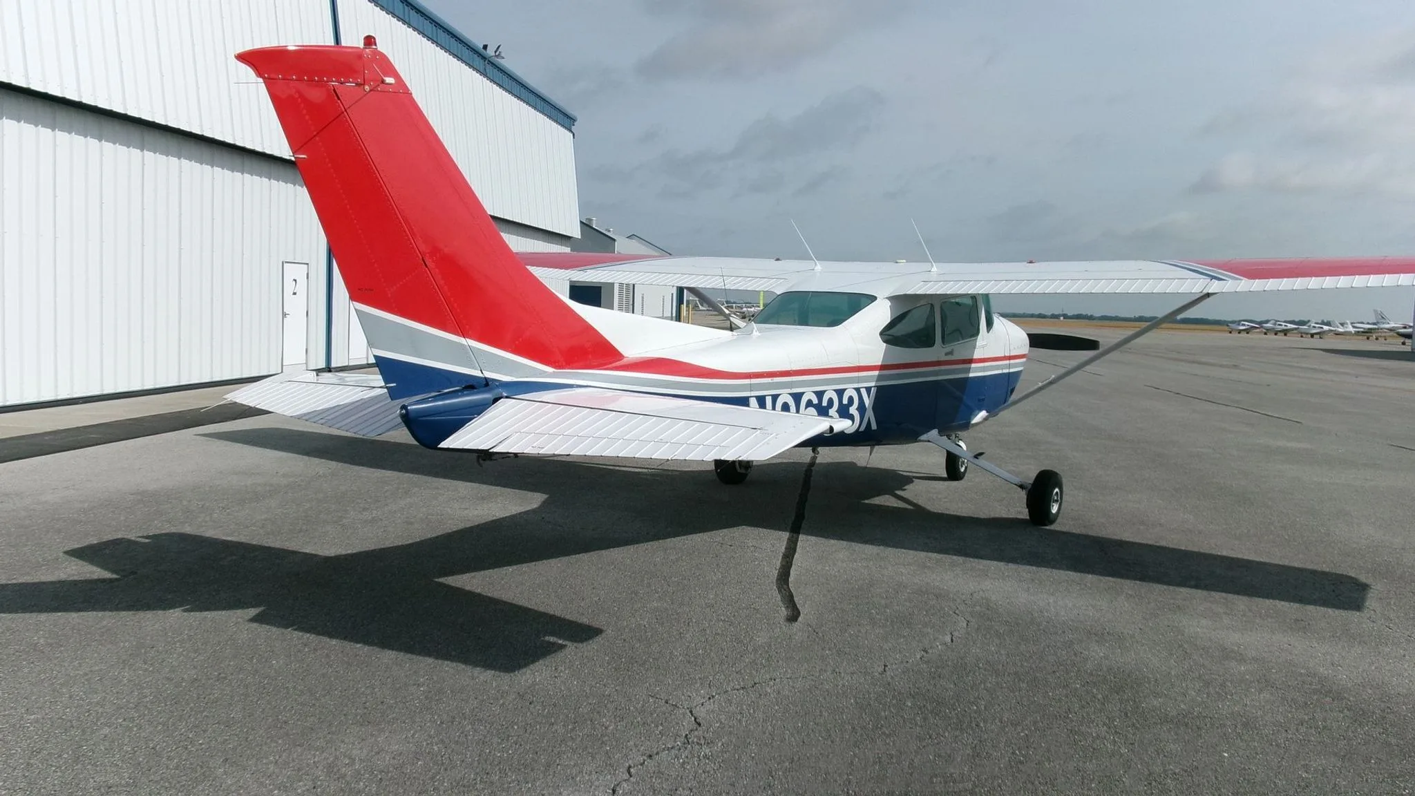 A rear view of a white, blue, and red Cessna 182 Skylane with registration N9633X parked on an asphalt apron.