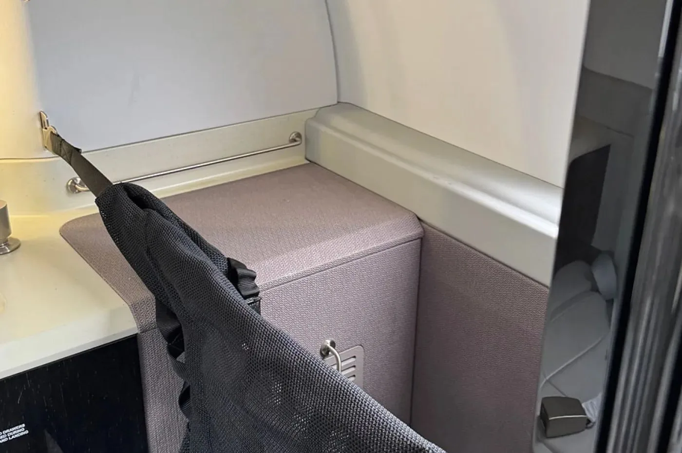 A detailed view of an aircraft interior storage compartment or lavatory area with a dark mesh bag hanging.