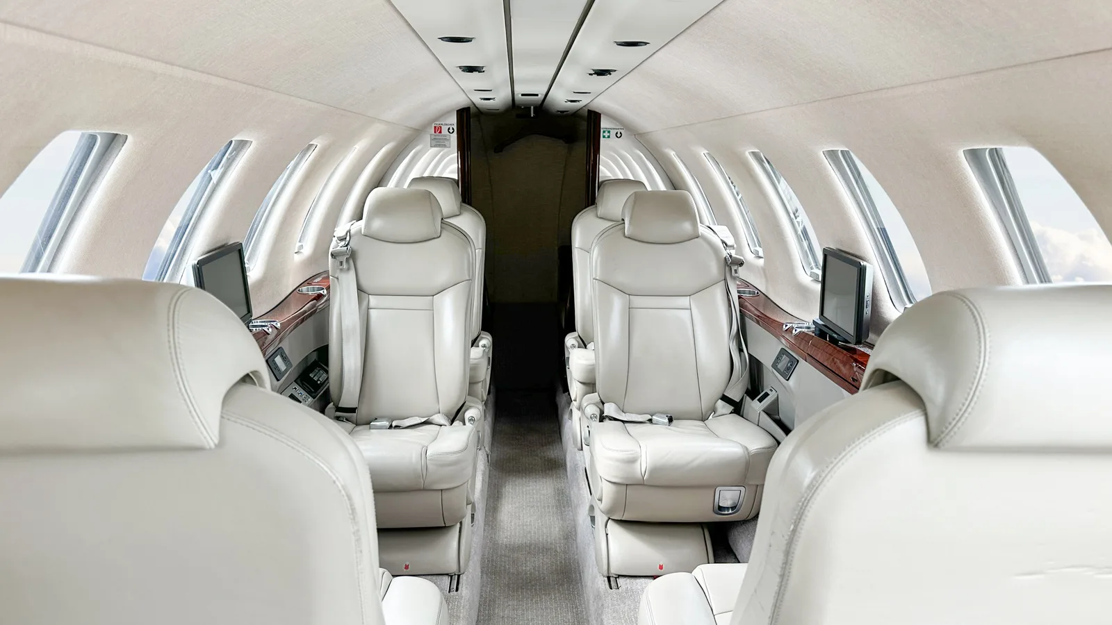 The luxurious beige leather interior cabin of a business jet, showing rows of seats and entertainment screens.