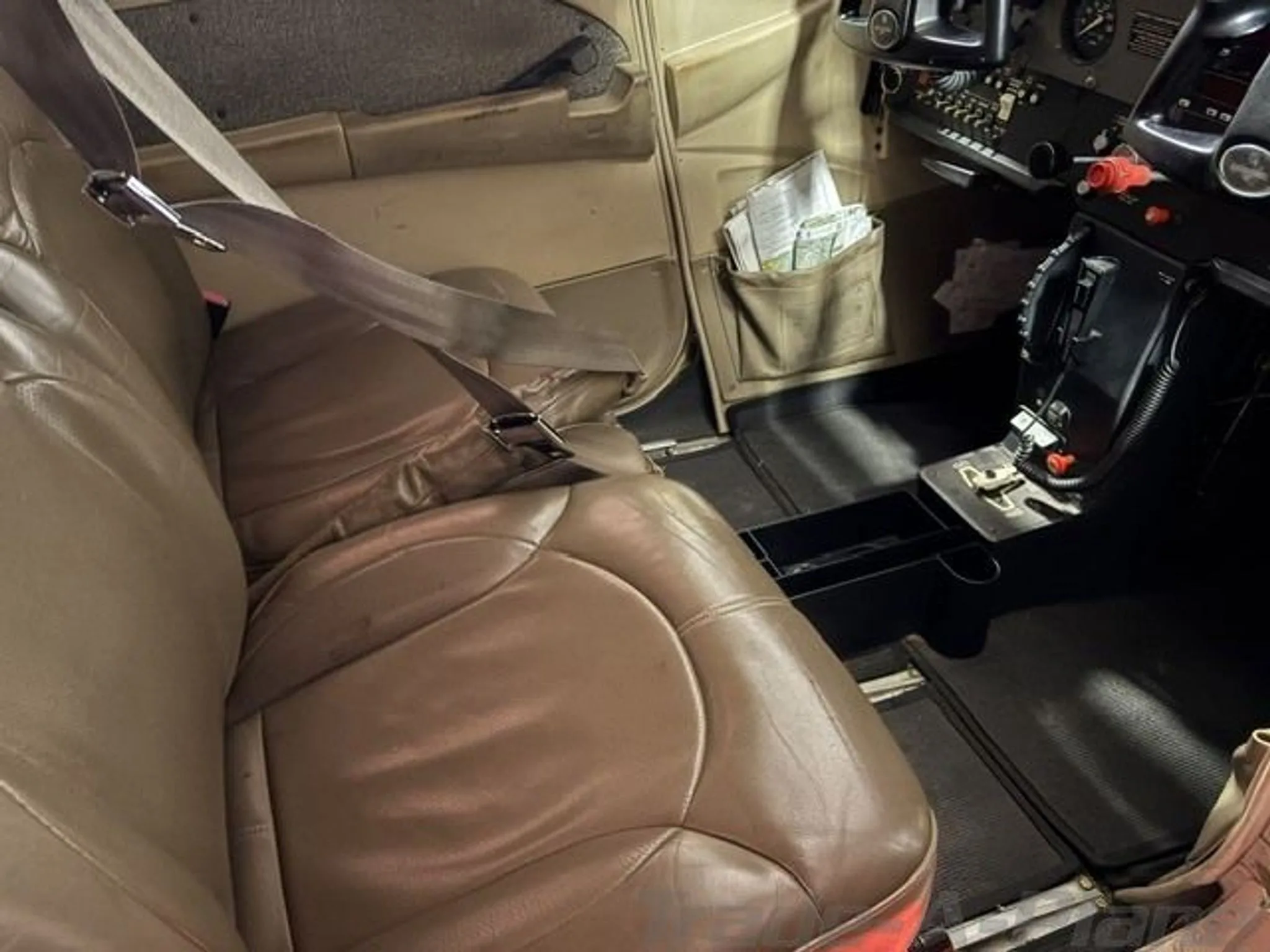 The tan leather front passenger seat and part of the cockpit controls of a small aircraft.
