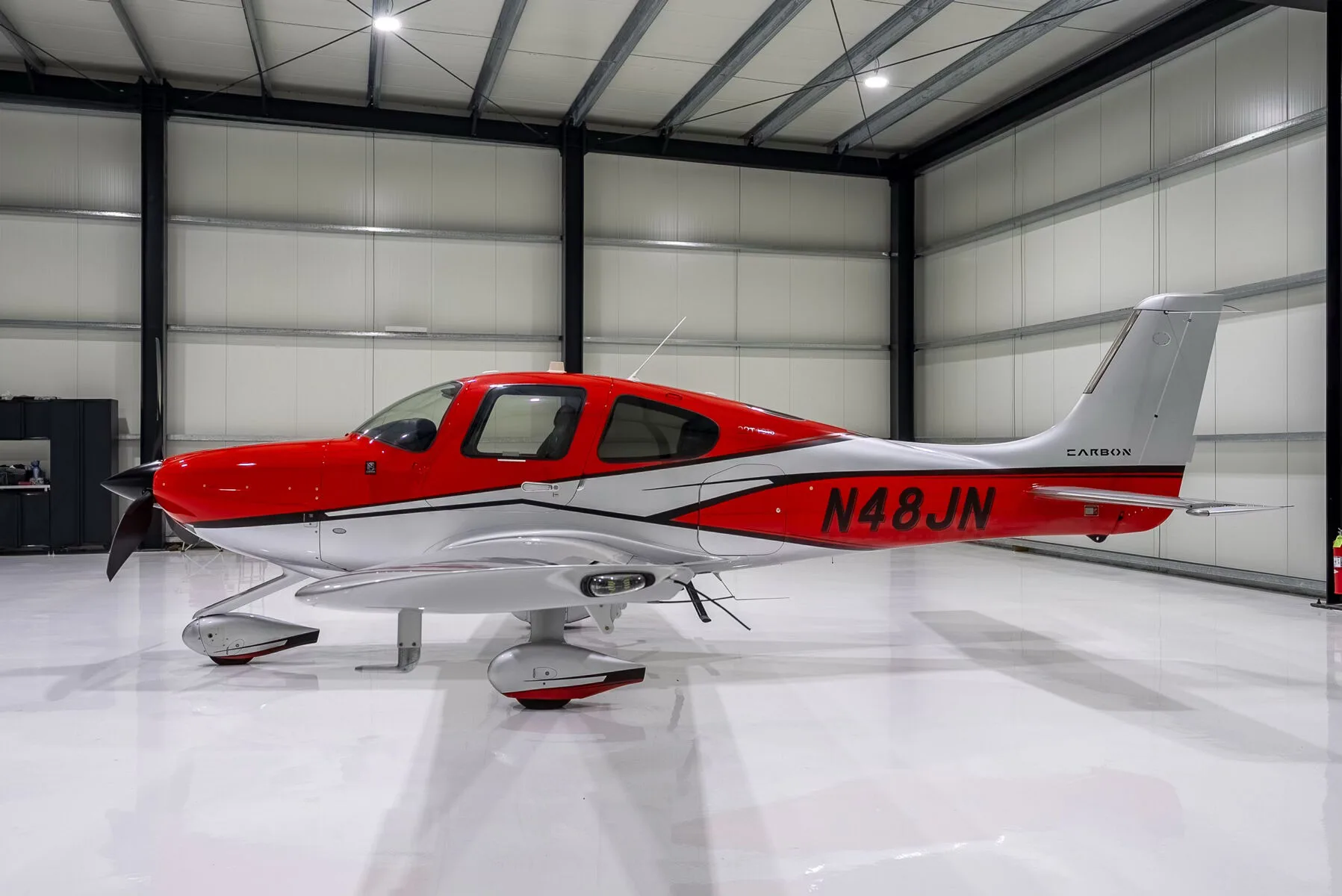 A red and silver Cirrus SR22T Carbon aircraft with registration N48JN parked in a hangar.