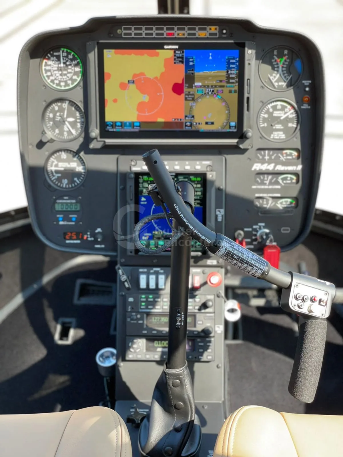 The cockpit of a Robinson R44 Raven II helicopter, showing the instrument panel with Garmin displays and flight controls.