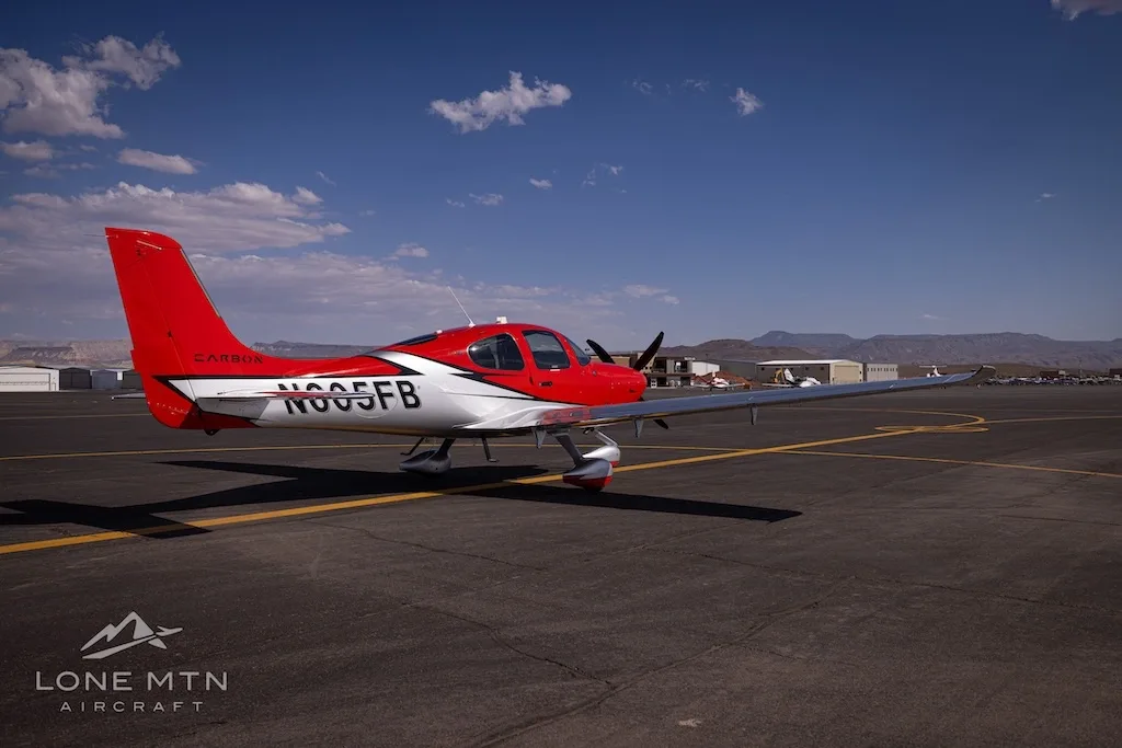 A rear-quarter view of a red and silver Cirrus SR22T aircraft (N605FB) on an airfield, showing the tail and registration.