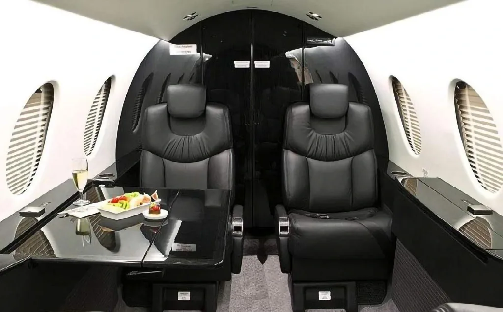 The luxurious black and white interior of a private jet cabin, featuring two facing black leather seats and a table with refreshments.