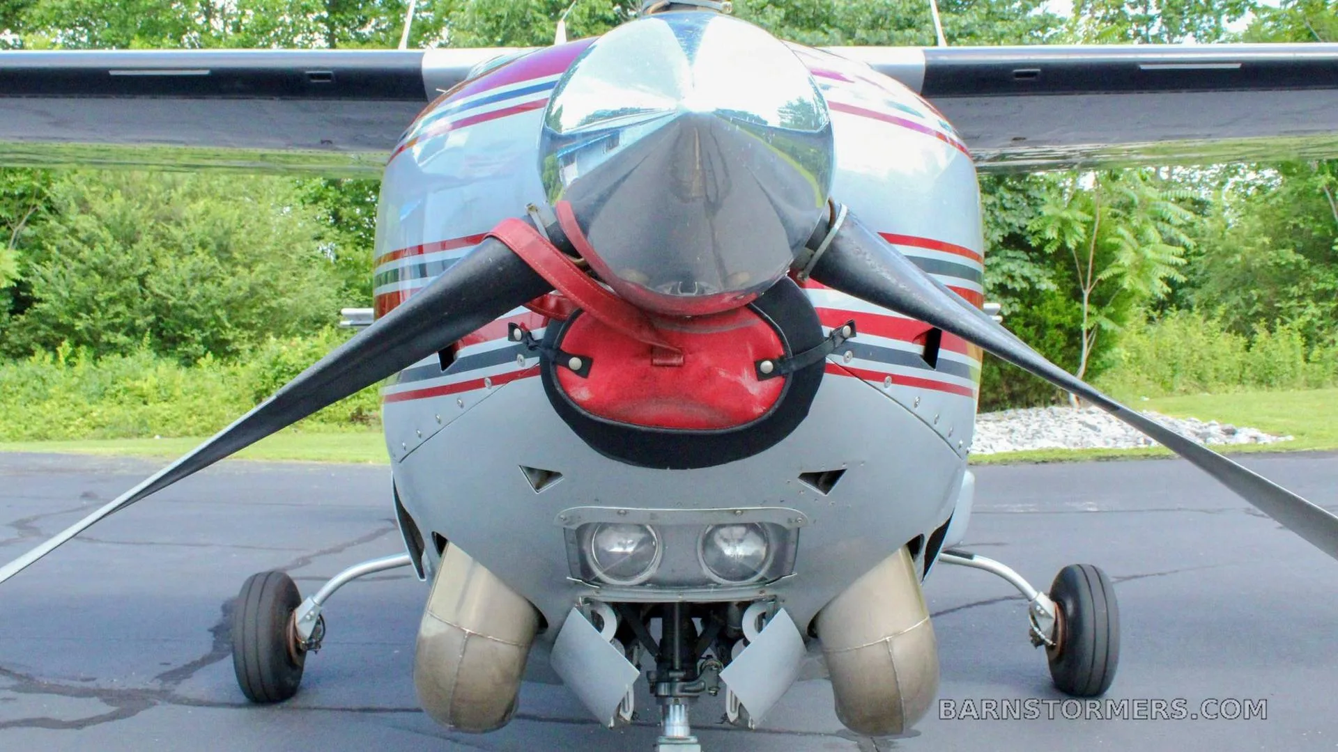 A close-up front view of a silver and red aircraft, showing its propeller, spinner, and engine cowling with landing lights.