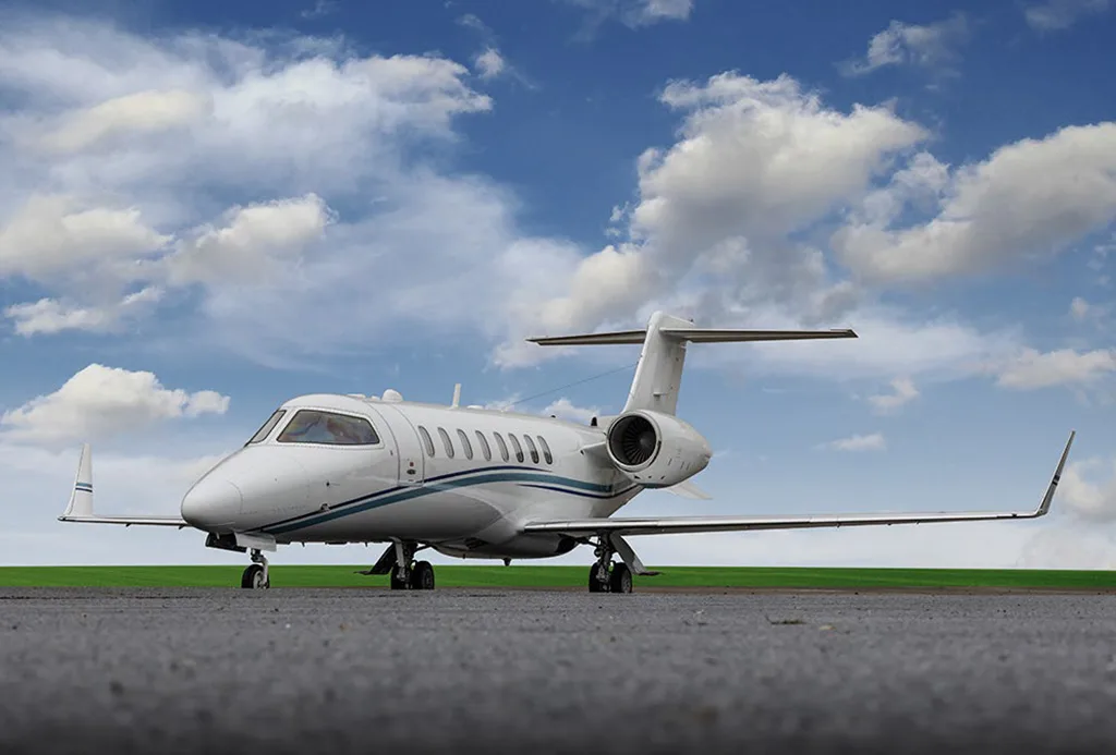 A white business jet with blue stripes parked on an asphalt runway under a cloudy blue sky.