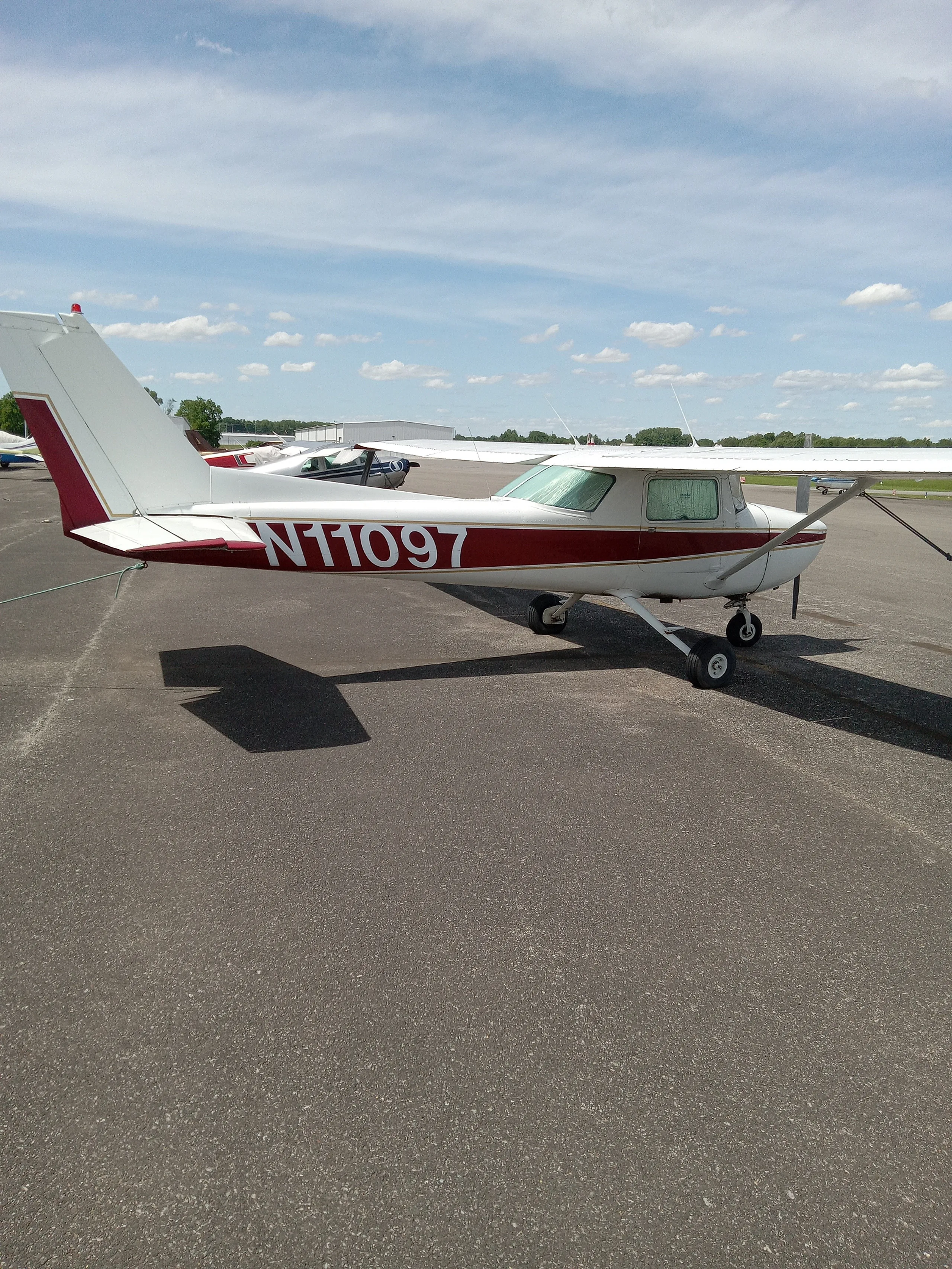 A white and maroon Cessna 150 or 152 aircraft, N11097, parked on an asphalt ramp under a partly cloudy sky.