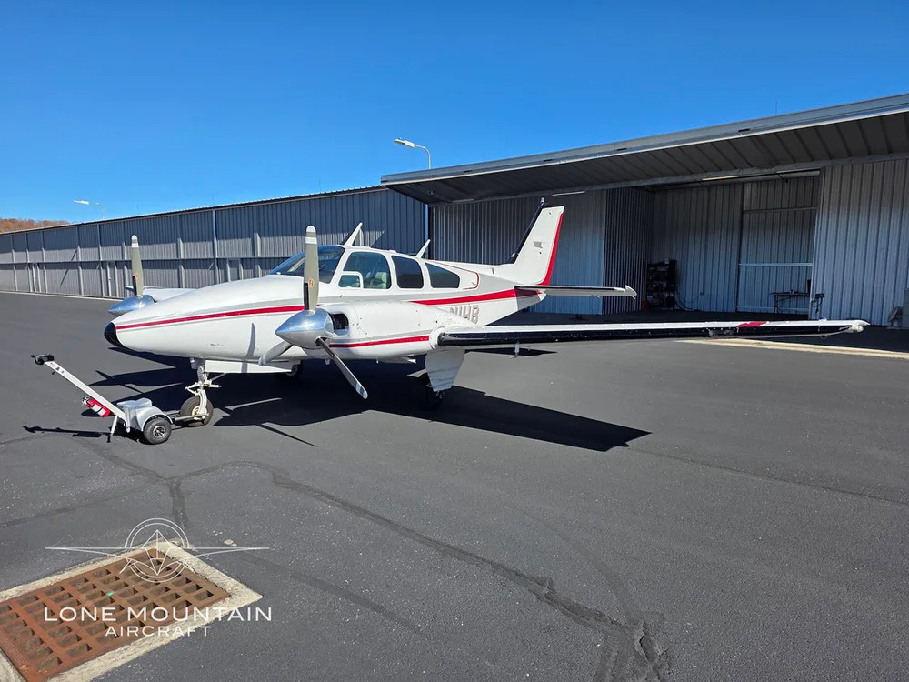 A white and red twin-engine aircraft, N1HB, is parked on an asphalt ramp next to a hangar.